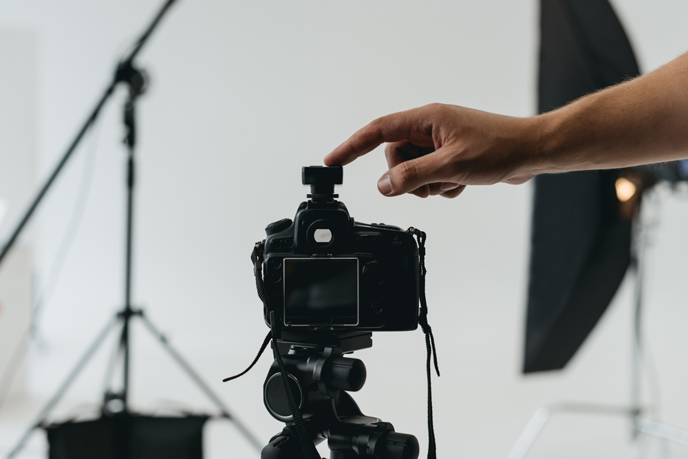 A close-up of a hand adjusting a camera on a tripod in a photography studio. The background is blurred, showing studio lights and equipment. | Studio 99 Multimedia